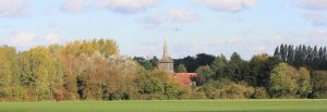 An autumn view across open farm land towards the bell tower of St Laurence church.